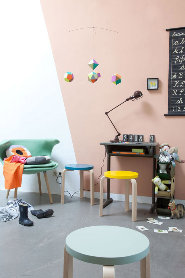Sala de juegos con pisos de madera diferentes colores. Pared bicolor blanco y rosa pálido dividida de manera vertical y en diagonal.