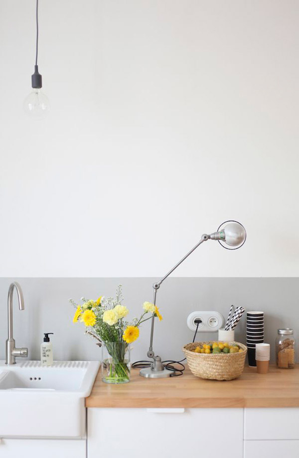 Vista de mesón de cocina con el lavaplatos en muebles blancos y cubierta de madera laminada color natural. Pared bicolor gris en parte inferior y blanco en la superior.