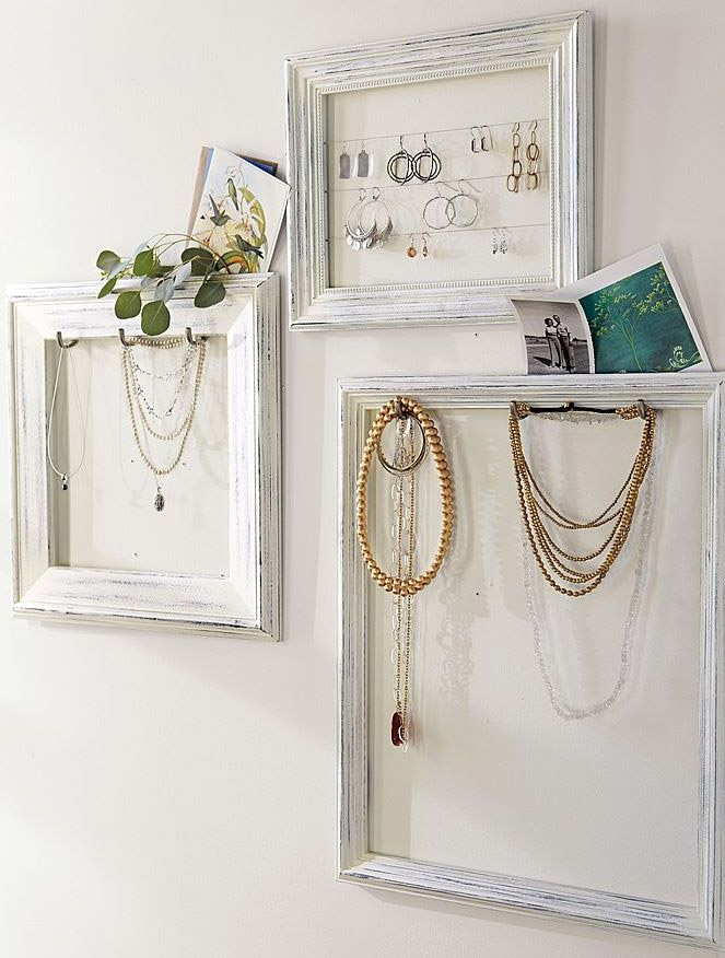 Tres marcos de foto blancos, unos con ganchos en los bordes internos para los collares y otro con hilos tensados para los aros.