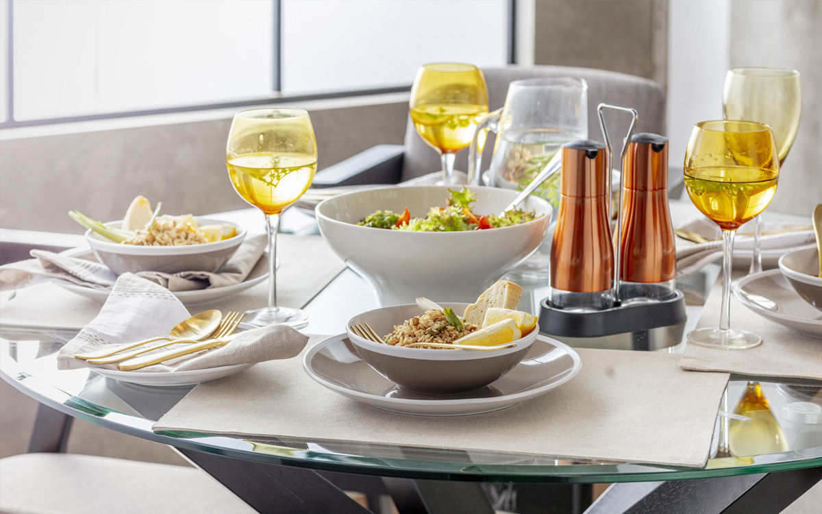 Detalle de mesa con individuales y vajilla, copas en color amarillo transparente y cubiertos dorados.