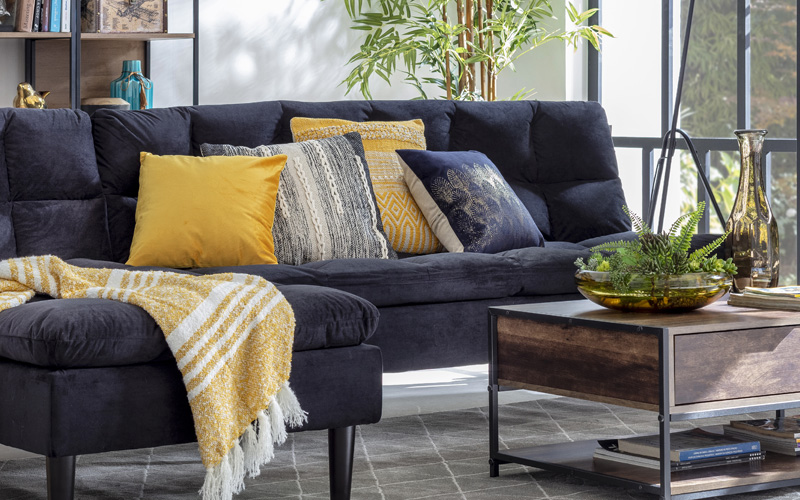 Sala de estar o living espacioso, con toques de estilo industrial, terciopelo y plantas, sillón oscuro con cojines color mostaza y mesa de centro estilo industrial.