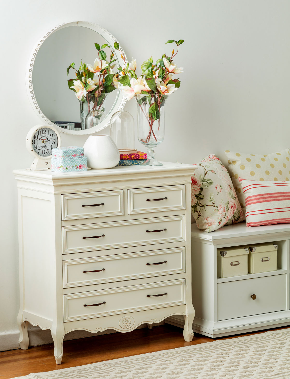 Recibidor con una cómoda blanca con cajones ambientado con detalles decorativos que incluyen un rack con cajas y cojines de distintos diseños
