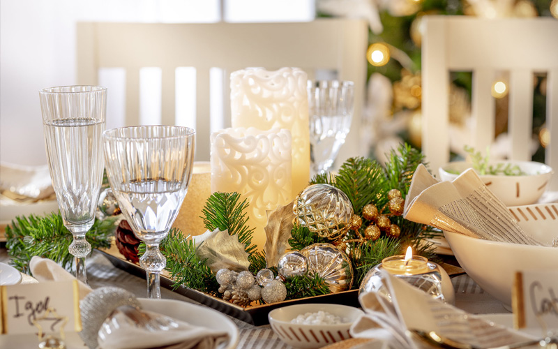 Detalle de mesa navideña con copas, velas, piñas de pino y vajilla dorada.
