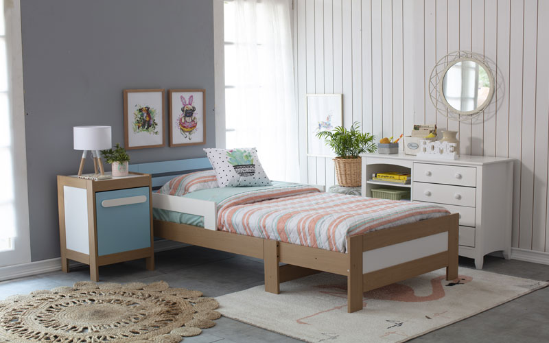 Imagen de parte superior de cama con almohada con colores coral, celestes y láminas decorativas en el muro