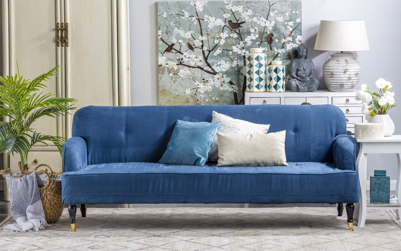 Living con estilo, con sofá azul, cojines blancos y celeste, mesa de arrimo, cuadro estilo oriental e imagen de buda sobre cajonera.